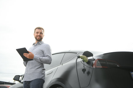 Full length portrait of young handsome bearded man in casual wear, standing at the charging station...