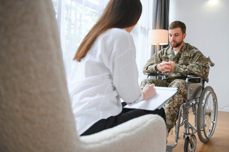 Depressed guy in camouflage uniform paralyzed soldier in wheelchair visiting female psychologistの写真素材