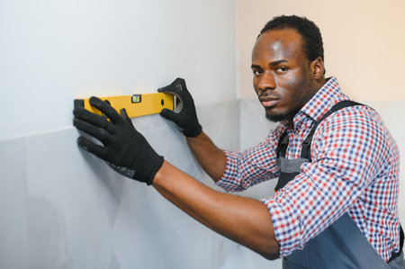 African American Worker installing wall tile with vacuum holder indoors.