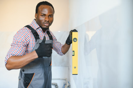 African American Worker installing wall tile with vacuum holder indoors.