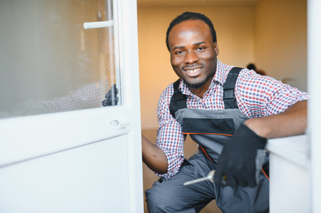 Young African Repairman In Overalls Installing Window.の写真素材
