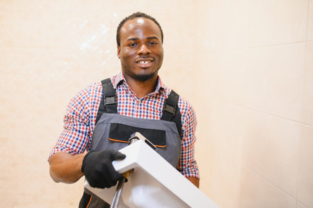 Side View Of Young African Male Plumber Fixing Sink In Bathroom.の写真素材