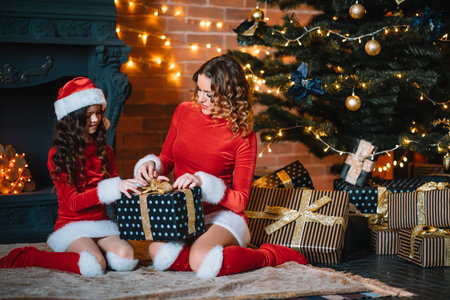 Merry Christmas and Happy Holidays! Cheerful mom and her cute daughter girl in Christmas costumes exchanging gifts.の写真素材