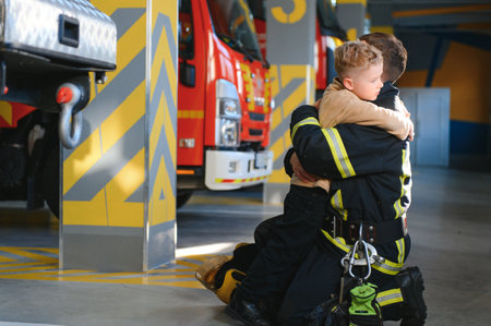A firefighter take a little child boy to save him. Fire engine car on background.の写真素材