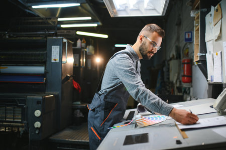 Print house worker controlling printing process quality and checking colors with magnifying glass.の写真素材