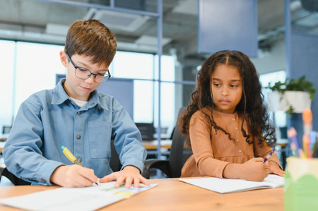 Focused multiracial students kids writing down data into notebook while sitting at table near classmates during test at schoolの写真素材