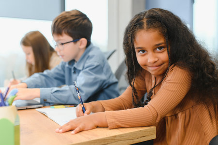 African American School Girl Writing Learning Sitting At Desk In Classroom Indoors. Diverse Children Having Class Taking Notes Indoor. Education And Knowledge. Selective Focusの写真素材