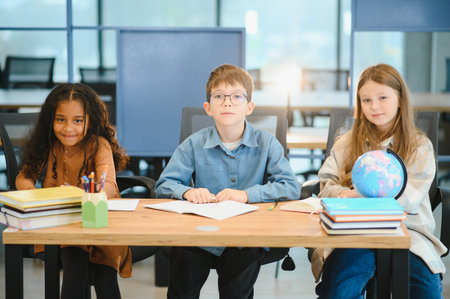 Focused multiracial students kids writing down data into notebook while sitting at table near classmates during test at schoolの写真素材