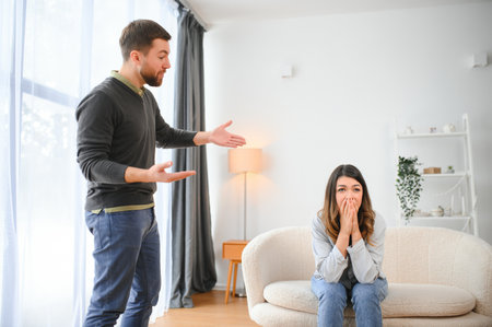 Emotional man gesturing and shouting at his wife, young couple having quarrel at home. Domestic abuse concept.の写真素材