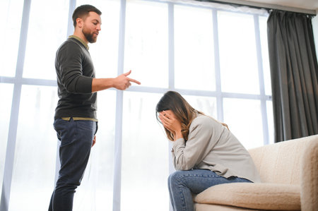 Irritated husband is shouting at his wife with violence. Woman is covering her face with fear.の写真素材
