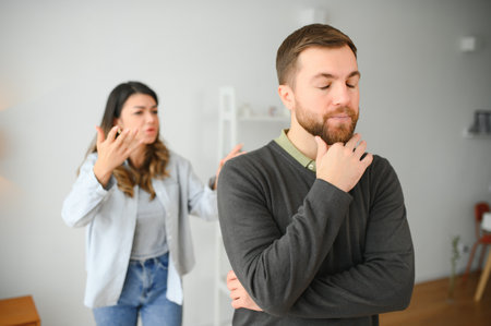 Couple arguing. Wife shouting to her desperate husband sitting on a couch in the living room at home.の写真素材