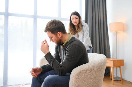 Couple arguing. Wife shouting to her desperate husband sitting on a couch in the living room at home.の写真素材