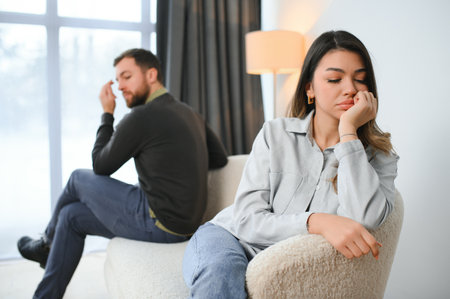 Beautiful couple is sitting back to back on the couch while having a quarrel.の写真素材