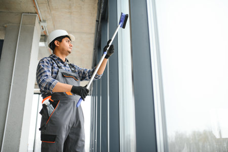 Male professional cleaning service worker cleans the windows and shop windows of a store with...
