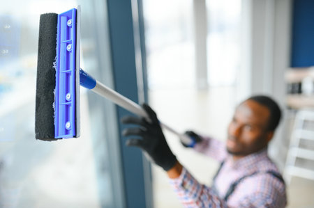 Happy Male Worker Cleaning Glass With Squeegee And Spray Bottle.