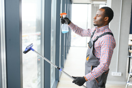 African Male professional cleaning service worker in overalls cleans the windows and shop windows of a store with special equipment.の写真素材