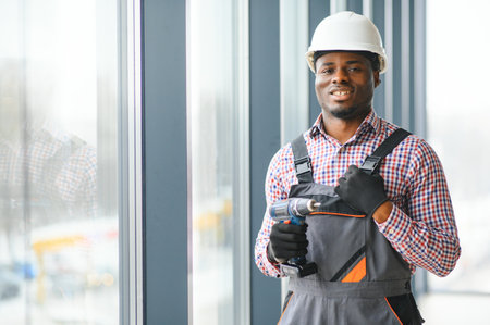 Low Angle View Of A Young African Repairman In Overalls Installing Window.の写真素材