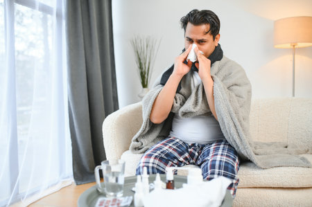 health, cold and people concept - sick young Indian man in blanket having headache or fever at home.の写真素材