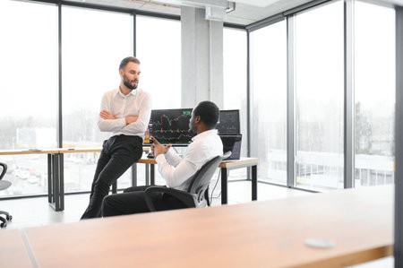 Two men colleagues traders sitting at desk at office monitoring stock market.