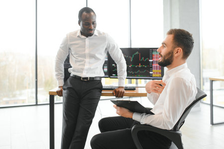 Two successful trader sitting in office, checking cryptocurrency information data on finance market graph, pointing on monitor.の写真素材
