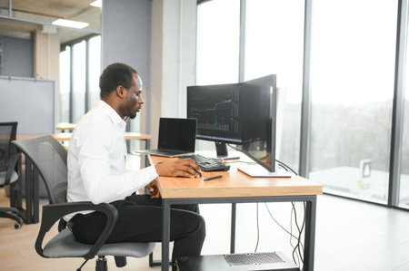 African American trader works at computer with displayed real-time stocks.