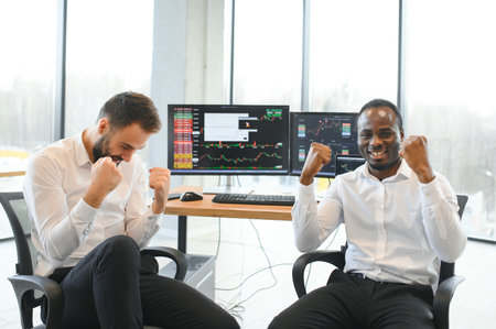 Two smiling confident businessmen, financial analysts or investment advisers sitting at office desk with laptop and documents, business analysis, consulting services, team portraitの写真素材