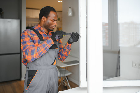 a African repairman repairs, adjusts or installs metal-plastic windows in the apartment.