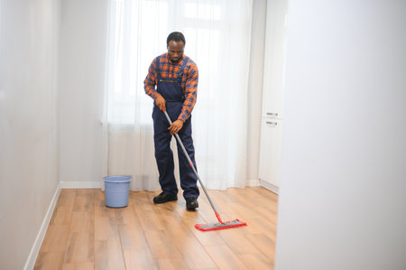 Young african man washes the floor with a mop in the room.