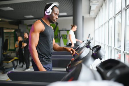Athletic man standing in a gym listening to music using wireless headphones.