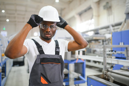 Portrait of industrial engineer. Smiling factory worker with hard hat standing in factory production line.の写真素材