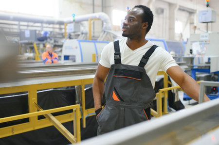 African male engineer standing in engine room to control a material production machine system,...