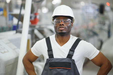 African male engineer standing in engine room to control a material production machine system,...