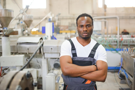 Portrait of African American male engineer in uniform and standing in industrial factory.