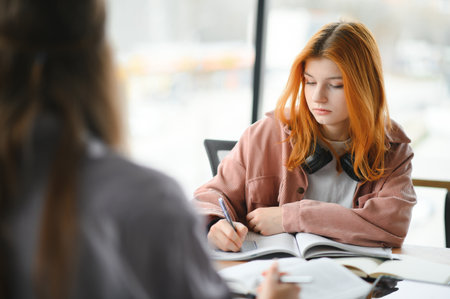 students sit at shared desk making notes studying together at university.の写真素材