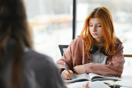students sit at shared desk making notes studying together at university.の写真素材