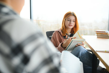 students sit at shared desk making notes studying together at university.の写真素材