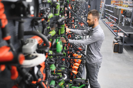 a man in a hardware store chooses a new screwdriver next to a showcase of power tools for repairs in...