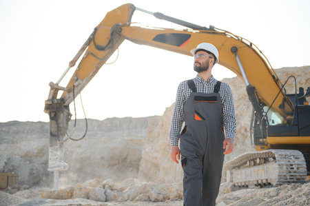 A worker in a helmet stands on the background of an excavator in a quarry.の写真素材