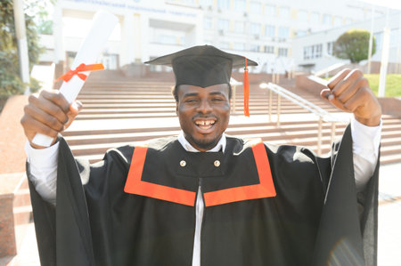 I have finally graduated. Happy young African man in graduation gowns holding diploma.の写真素材