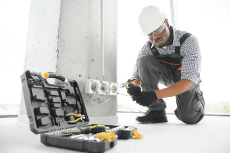 African American electrician replacing socket in room.の写真素材