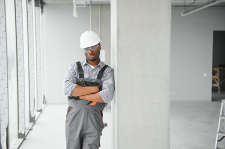 Portrait of handsome young African American male builder in hard hat, working at construction site.
