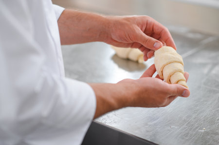 A male baker makes croissants in the bakery kitchen.