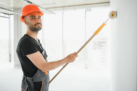 Portrait of man holding paint roller while painting white wall and making renovation.