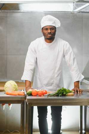 Experienced professional African-American chef standing in kitchen of restaurant with working staff.