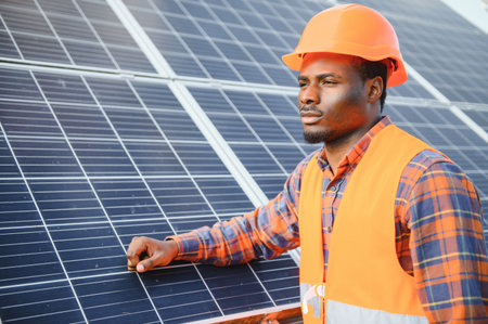African american man in safety helmet on solar panels with screwdriver. Competent technician using tools while performing service work on station.の写真素材