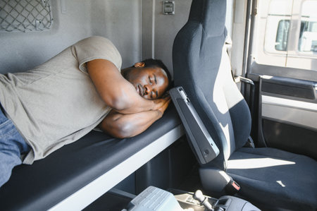 Truck driver sleeping in his cabin after working long routes overtime. Sleepy trucker taking a nap on a bed inside truck transporter. Lack of sleep.の写真素材