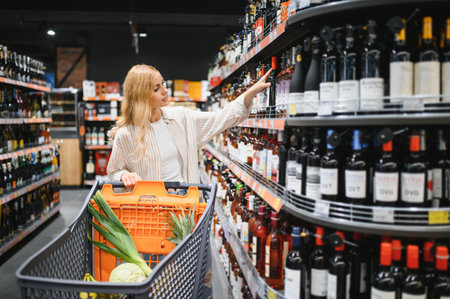 girl chooses wine in supermarket. girl reads labels on bottles of wine in supermarket.の写真素材