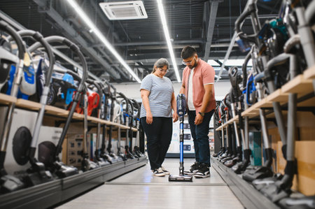 Young beautiful Indian couple buying new vacuum cleaner at tech store.の写真素材
