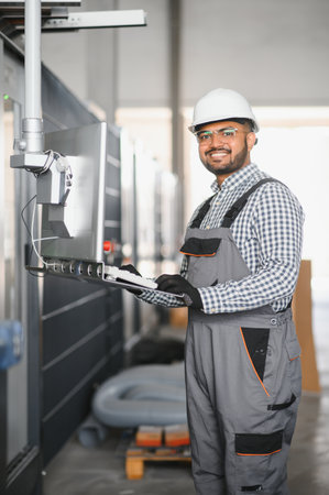 Happy Young Indian male engineer wearing safety workwear standing in the factory.