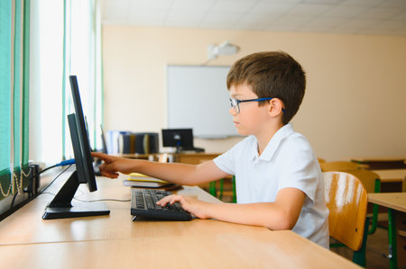 Teenage boy smiling while using computer at desk in classroom.の写真素材